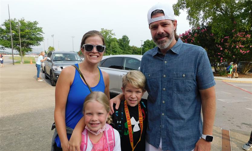 A family smiles in front of an elementary school